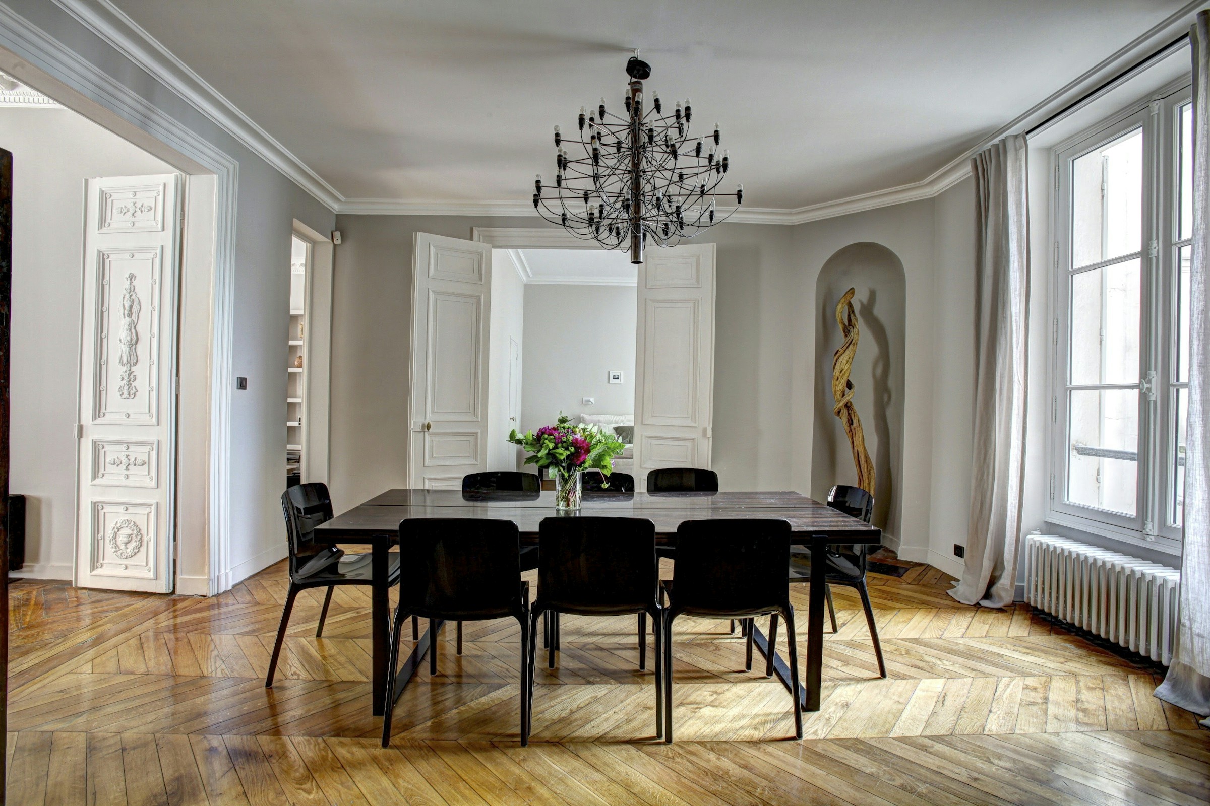 Intérieur parisien lumineux avec parquet, moulures et grandes fenêtres